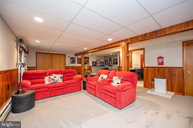 carpeted living room with baseboard heating, wood walls, and a drop ceiling