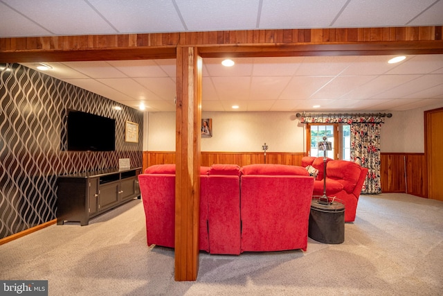 carpeted living room with a drop ceiling and wood walls