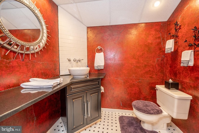 bathroom featuring tile walls, lofted ceiling, toilet, and vanity