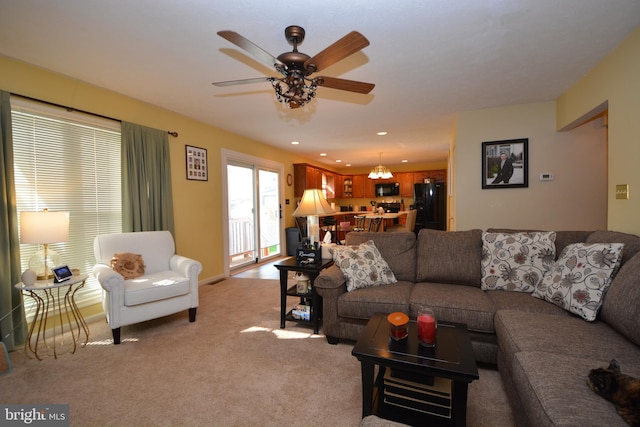 living room featuring ceiling fan with notable chandelier and light colored carpet