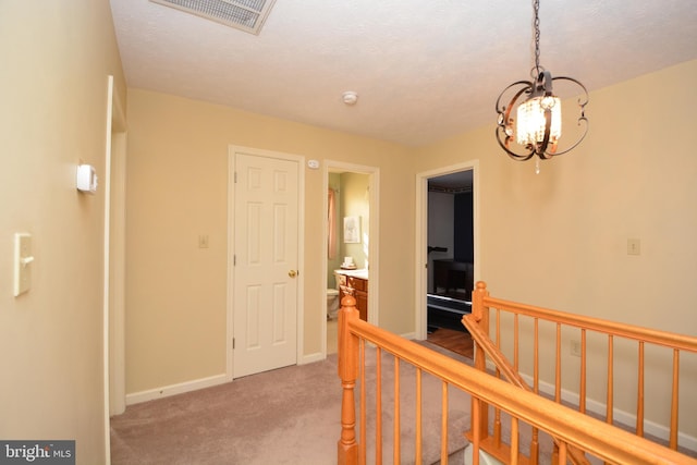 corridor with an inviting chandelier, light colored carpet, and a textured ceiling