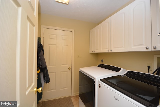 laundry area featuring a textured ceiling, washer and clothes dryer, and cabinets