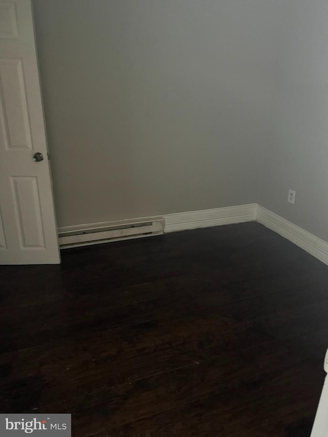 empty room with baseboard heating and dark hardwood / wood-style flooring