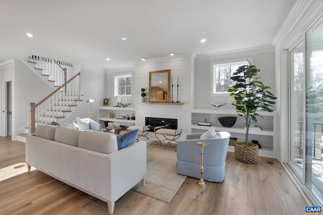 living room with a large fireplace, light hardwood / wood-style floors, and crown molding