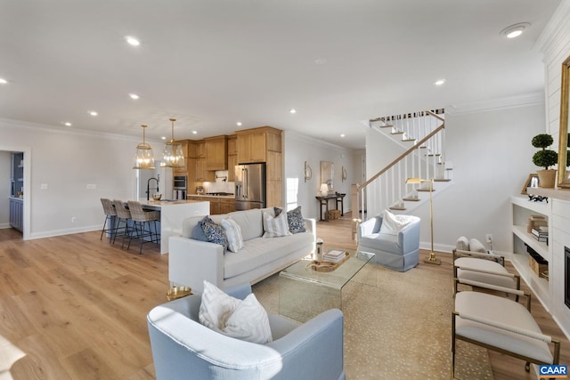 living room with sink, light wood-type flooring, crown molding, and a notable chandelier