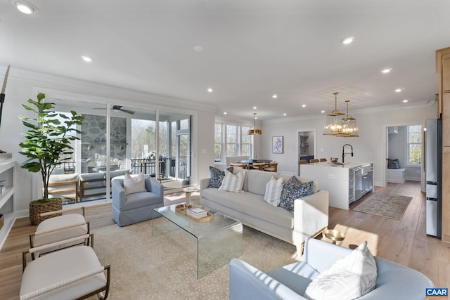 living room featuring ornamental molding, ceiling fan with notable chandelier, light hardwood / wood-style floors, and sink