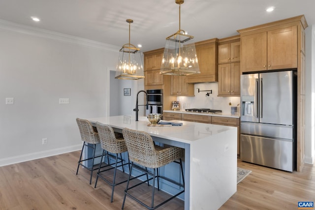 kitchen featuring pendant lighting, stainless steel appliances, an island with sink, and light hardwood / wood-style flooring