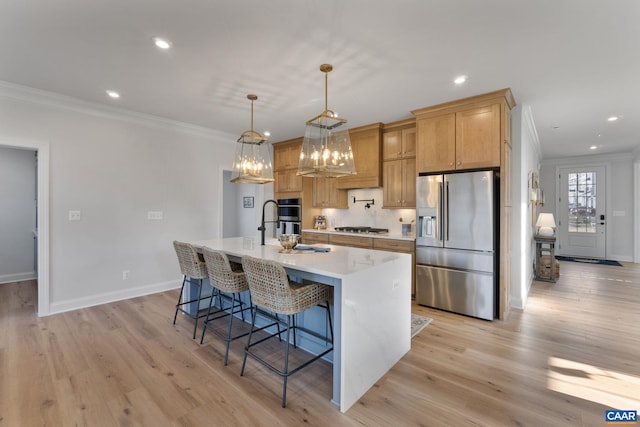 kitchen featuring crown molding, appliances with stainless steel finishes, pendant lighting, an island with sink, and light hardwood / wood-style flooring