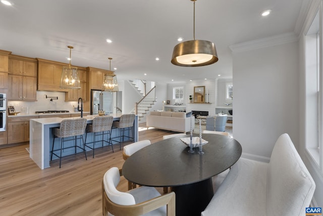 dining space with a fireplace, sink, light hardwood / wood-style floors, and crown molding