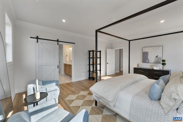 bedroom with a barn door, connected bathroom, light hardwood / wood-style flooring, and crown molding