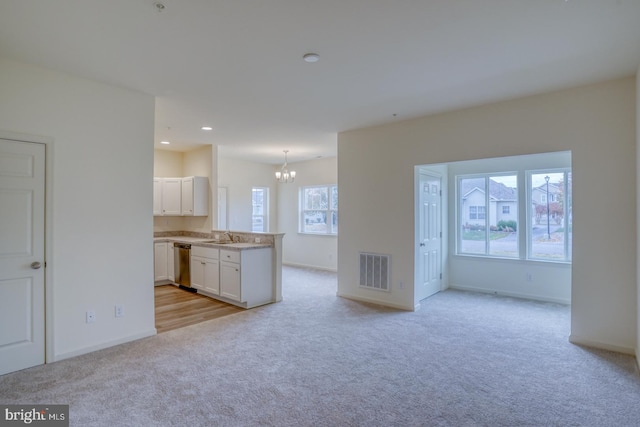 unfurnished living room with sink, light colored carpet, and a notable chandelier