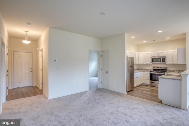 kitchen with white cabinets, stainless steel appliances, hanging light fixtures, and light carpet