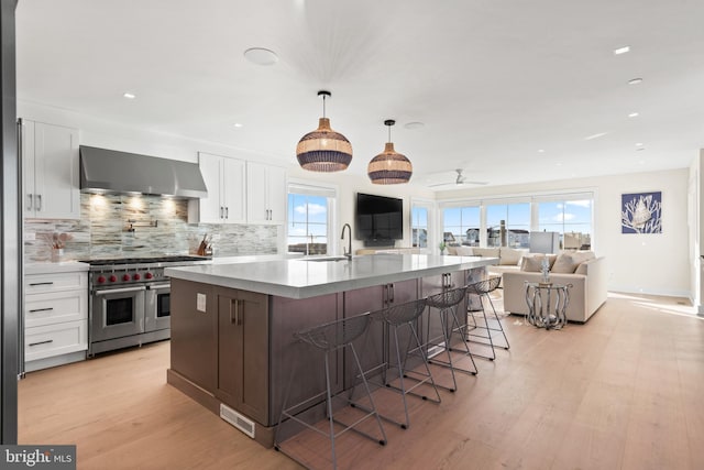 kitchen featuring white cabinets, wall chimney exhaust hood, range with two ovens, and a center island with sink