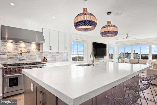 kitchen featuring a healthy amount of sunlight, white cabinetry, premium stove, and wall chimney range hood