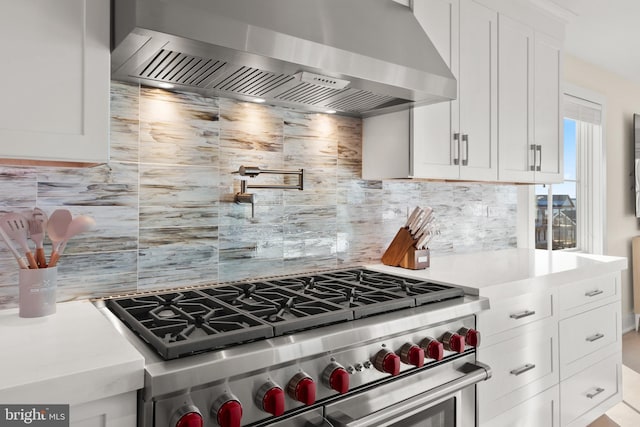 kitchen featuring high end range, white cabinets, decorative backsplash, and wall chimney exhaust hood