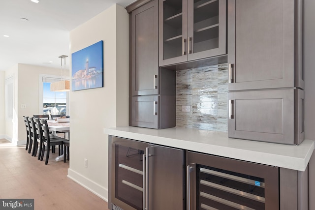 bar featuring decorative backsplash, light hardwood / wood-style floors, decorative light fixtures, and beverage cooler