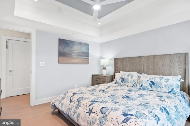 bedroom featuring a raised ceiling, ceiling fan, and light hardwood / wood-style floors