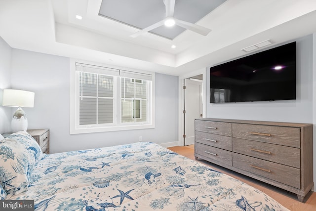 bedroom featuring ceiling fan, light wood-type flooring, and a tray ceiling