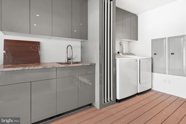 clothes washing area featuring cabinets, light hardwood / wood-style floors, washer and clothes dryer, sink, and electric panel