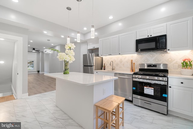 kitchen with sink, appliances with stainless steel finishes, backsplash, a kitchen island, and white cabinets