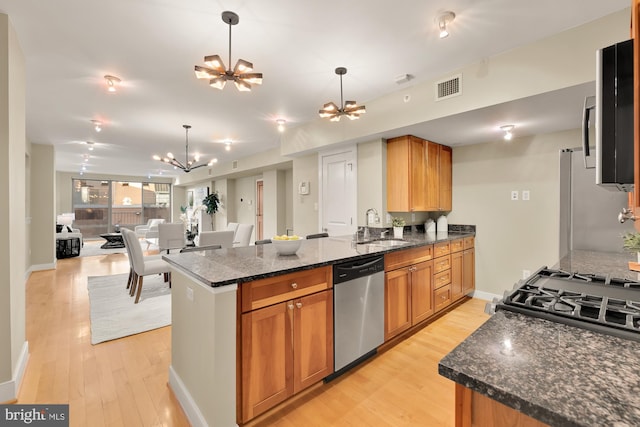 kitchen with stainless steel appliances, dark stone countertops, sink, and light wood-type flooring