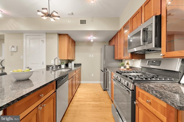 kitchen with dark stone counters, appliances with stainless steel finishes, sink, and light hardwood / wood-style floors