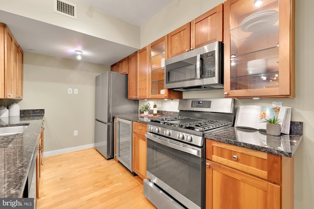 kitchen featuring wine cooler, light wood-type flooring, dark stone countertops, and stainless steel appliances