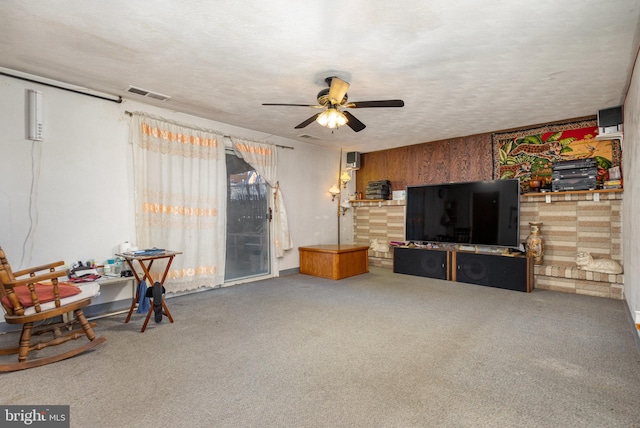 living room with a textured ceiling, carpet floors, ceiling fan, and wooden walls