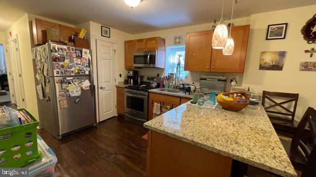 kitchen with light stone countertops, sink, hanging light fixtures, stainless steel appliances, and dark hardwood / wood-style floors