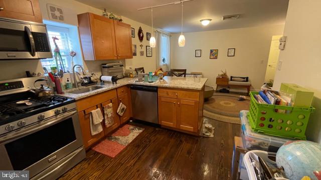 kitchen with hanging light fixtures, sink, appliances with stainless steel finishes, dark hardwood / wood-style flooring, and kitchen peninsula