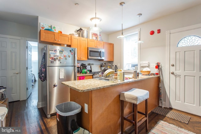 kitchen with kitchen peninsula, light stone countertops, hanging light fixtures, and appliances with stainless steel finishes