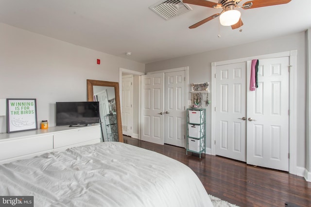 bedroom with ceiling fan, dark wood-type flooring, and two closets