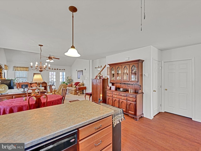 kitchen with light wood-type flooring, black dishwasher, hanging light fixtures, an inviting chandelier, and lofted ceiling