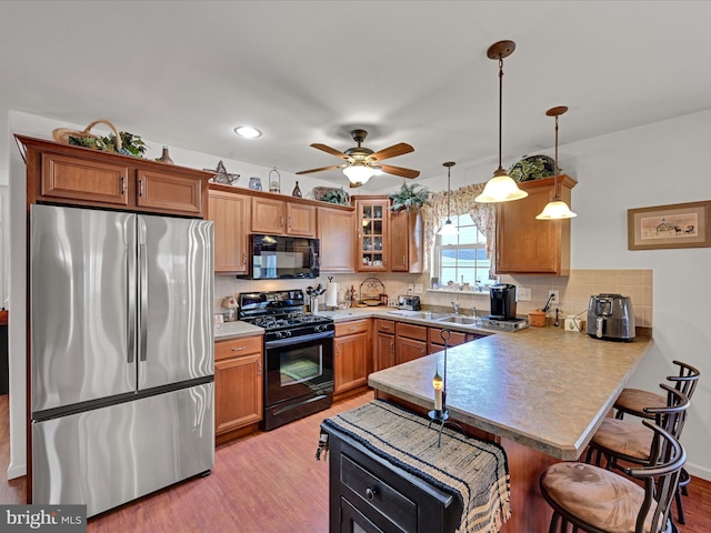 kitchen with kitchen peninsula, black appliances, a kitchen breakfast bar, pendant lighting, and light wood-type flooring