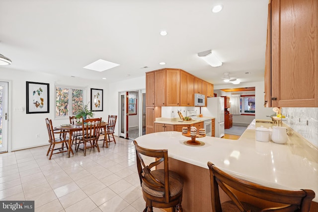 kitchen featuring kitchen peninsula, light tile patterned floors, backsplash, a skylight, and white appliances