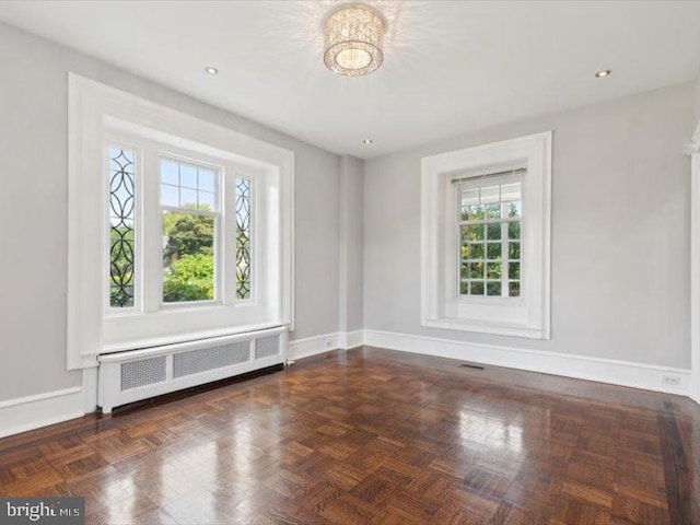 unfurnished room featuring radiator, plenty of natural light, and dark parquet floors