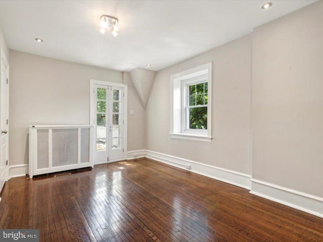 spare room featuring radiator heating unit, a healthy amount of sunlight, and dark hardwood / wood-style floors