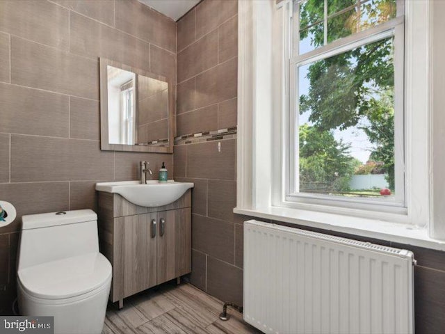 bathroom with radiator heating unit, vanity, tile walls, and a healthy amount of sunlight