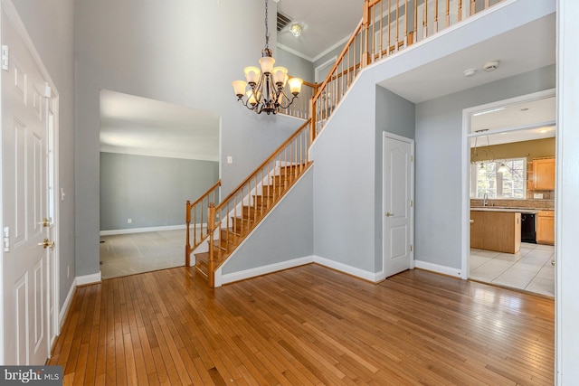 foyer entrance with ornamental molding, an inviting chandelier, light hardwood / wood-style floors, and a towering ceiling