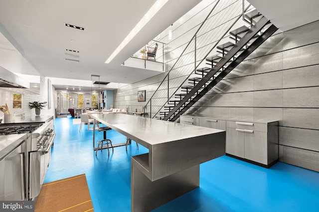 interior space with a breakfast bar, high end stainless steel range oven, hanging light fixtures, decorative backsplash, and a kitchen island