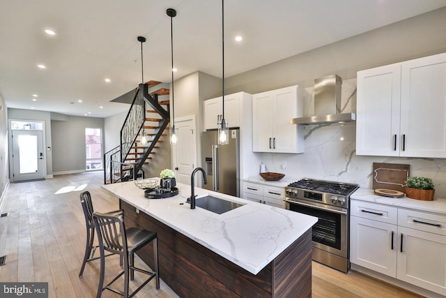 kitchen featuring wall chimney range hood, white cabinets, a center island with sink, and stainless steel appliances