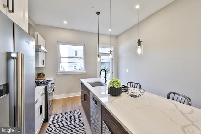 kitchen with a kitchen bar, white cabinets, hanging light fixtures, light stone countertops, and appliances with stainless steel finishes