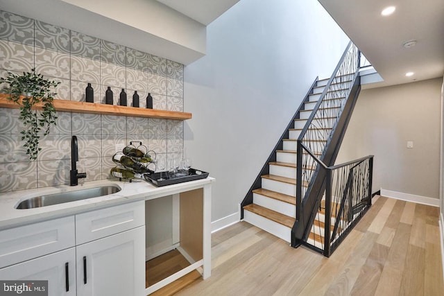 bar featuring light stone counters, backsplash, light wood-type flooring, sink, and white cabinets