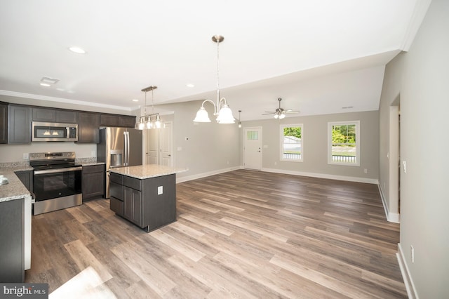 kitchen with appliances with stainless steel finishes, light stone countertops, hardwood / wood-style floors, dark brown cabinets, and a center island