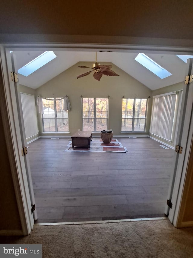 interior space featuring wood-type flooring, ceiling fan, and vaulted ceiling with skylight