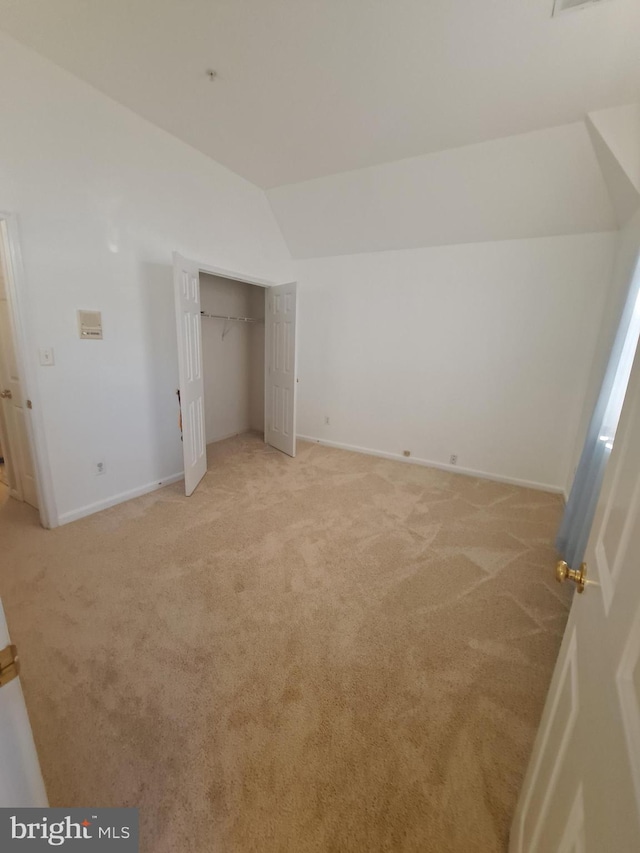 unfurnished bedroom featuring a closet, light colored carpet, and lofted ceiling