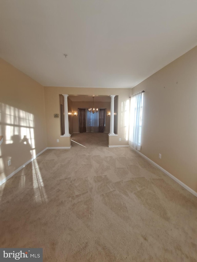 carpeted empty room with decorative columns and a chandelier