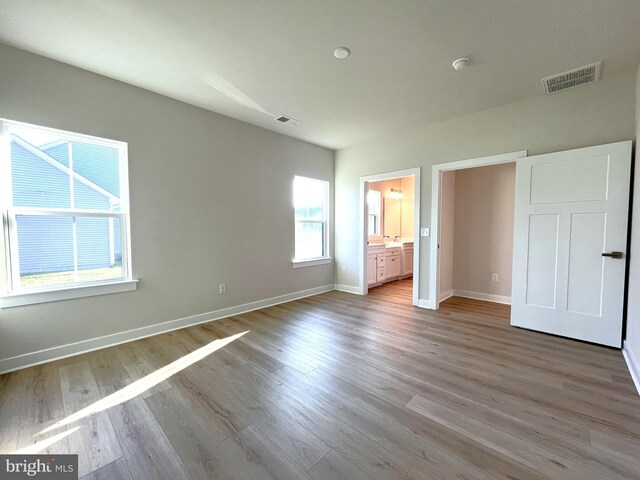 unfurnished bedroom with ensuite bathroom and light hardwood / wood-style floors