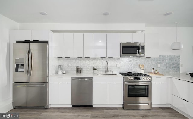 kitchen featuring wood-type flooring, stainless steel appliances, hanging light fixtures, sink, and white cabinets