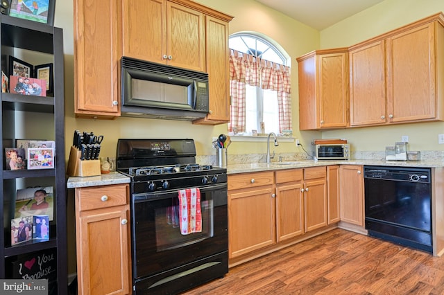 kitchen with black appliances, light wood-type flooring, sink, and light stone countertops